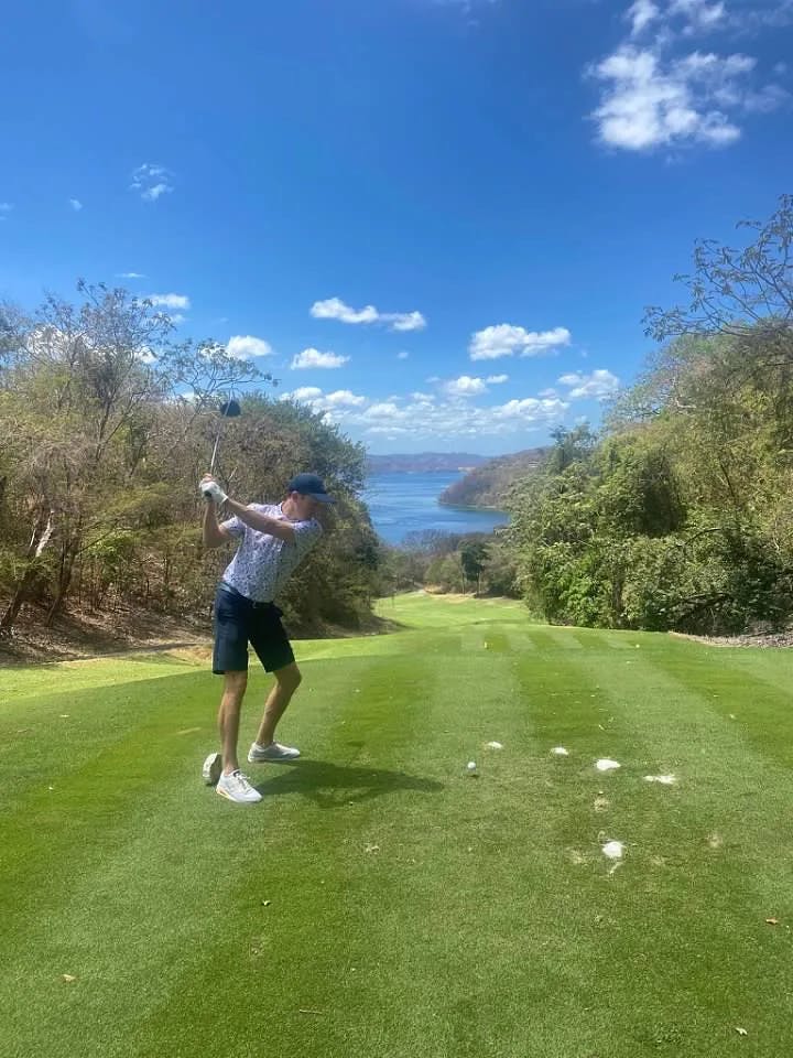 A man golfing on a golf course next to the water.
