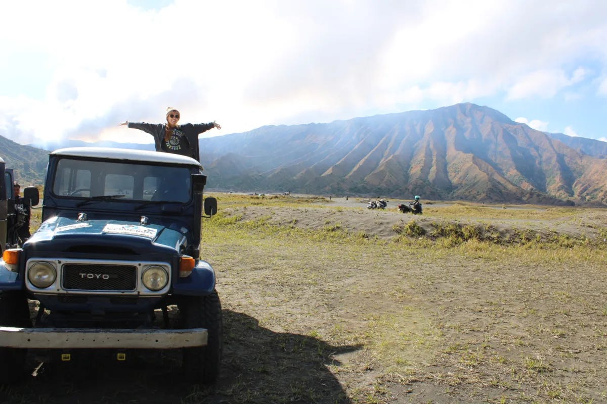 Isabel posing on top of a truck with her arms outstretched and a mountain the background.