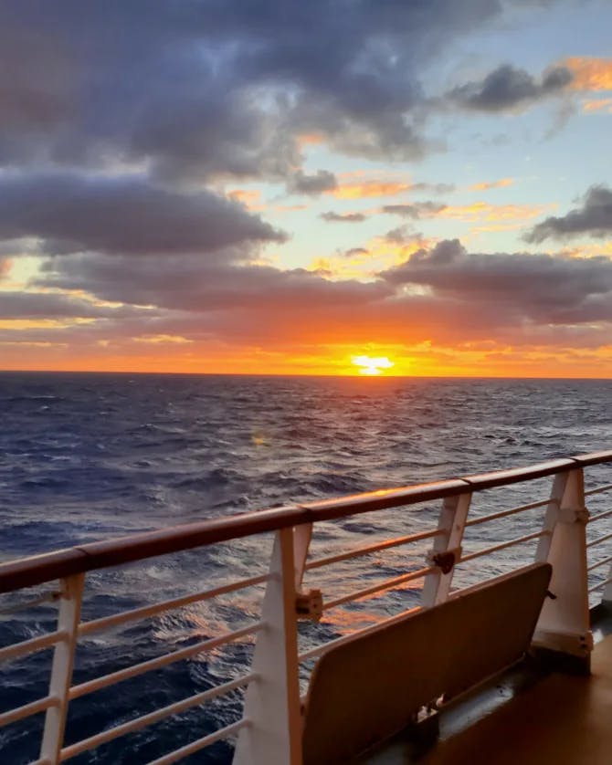 A view of a sunset over the ocean from a ship deck 