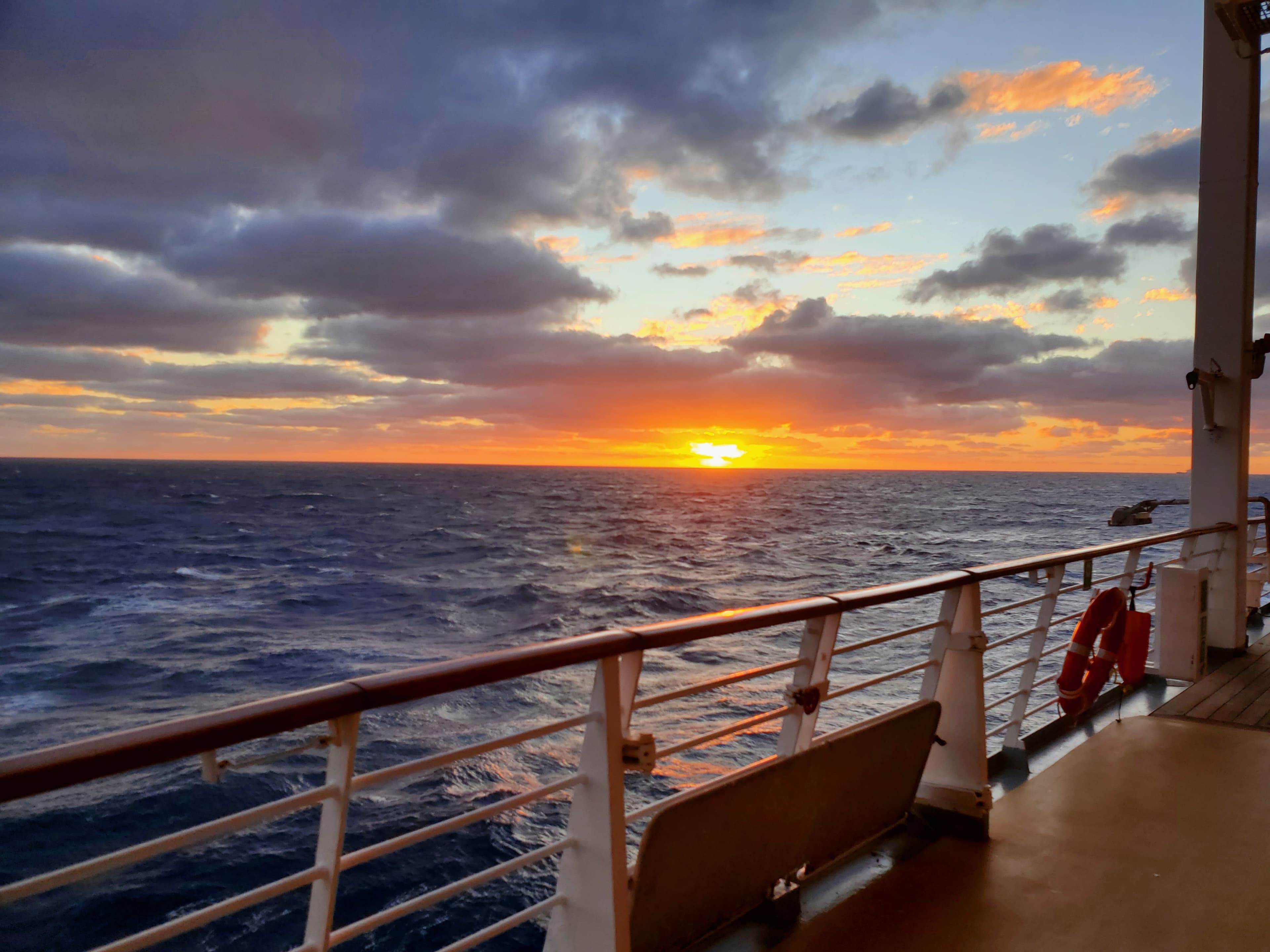 A view of a sunset over the ocean from a ship deck