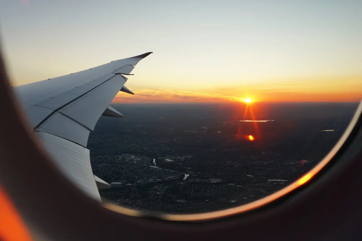 The sun sets over an urban skyline bisected by a river, all seen from the window of a plane