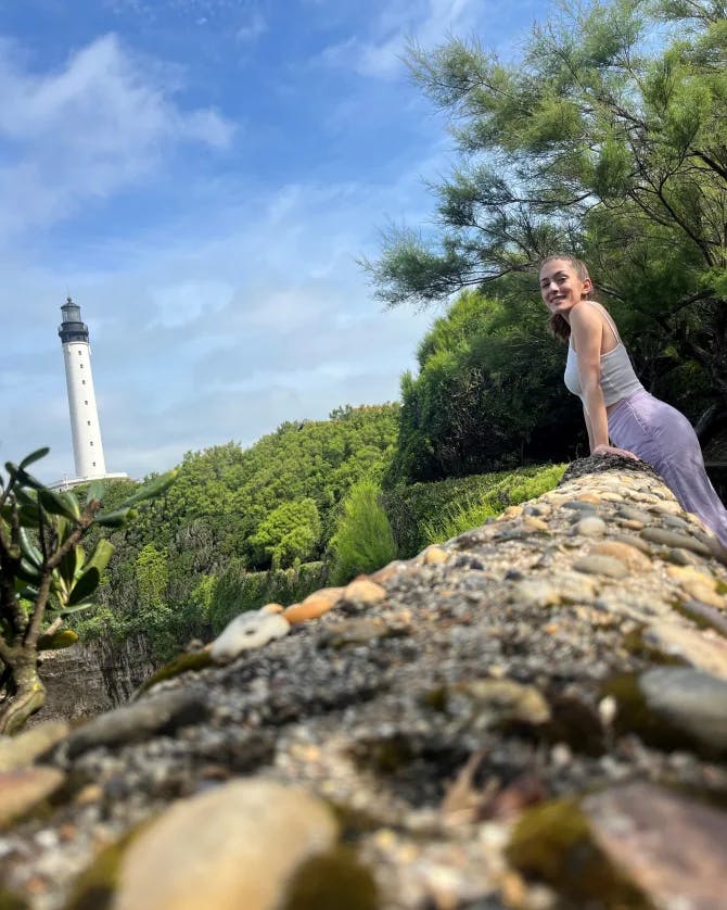 Stephanie posing against a rocky ledge with trees and a white lighthouse in the background.