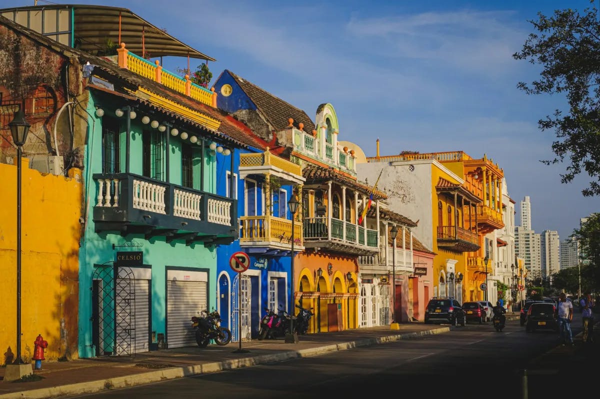 Colorful, Old World-style buildings line a street in Getsemani, Cartagena with the urban skyline faintly visible in the distance