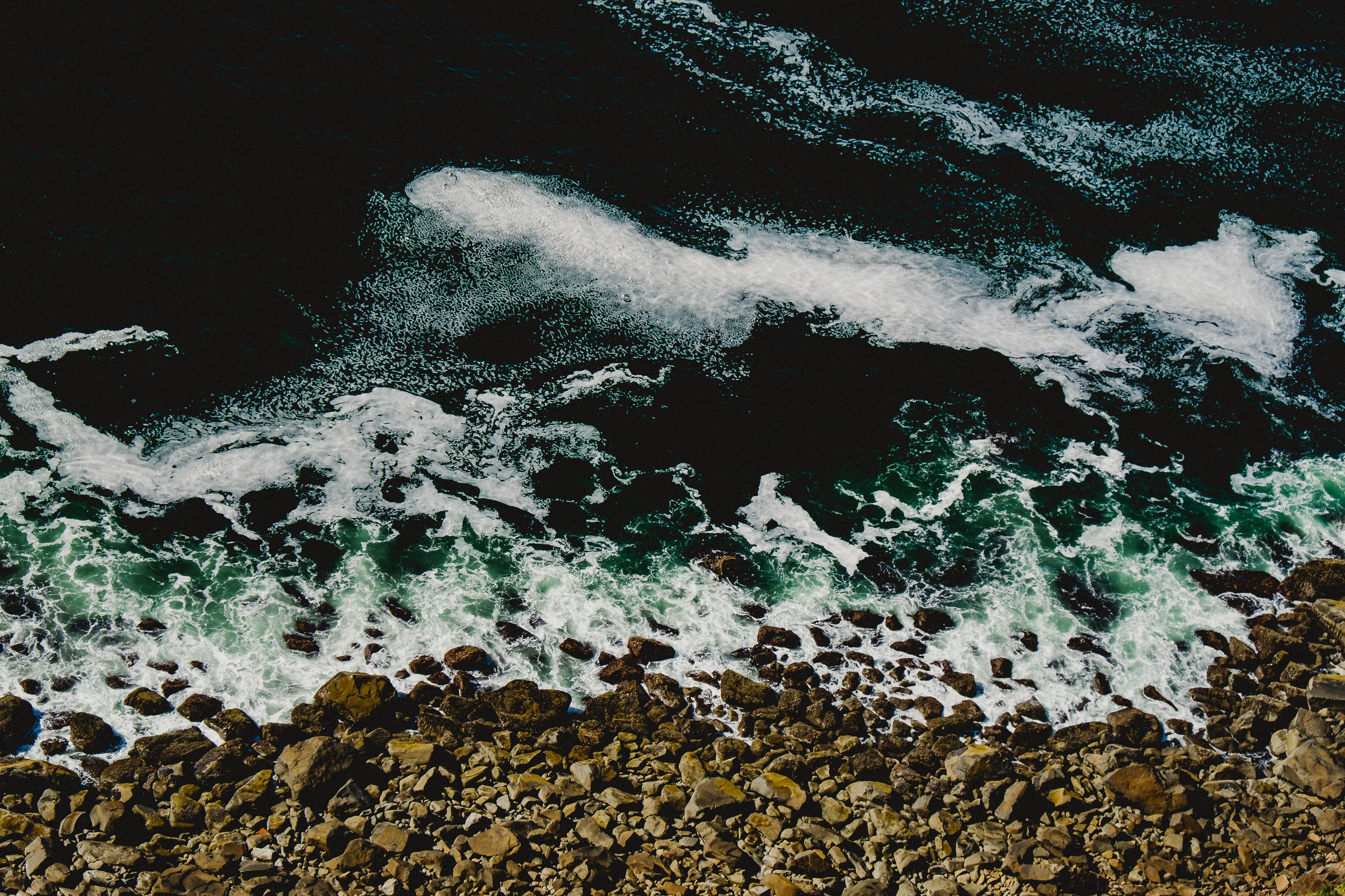 Close-up perspective taken from above of waves crashing against a rocky coastline.