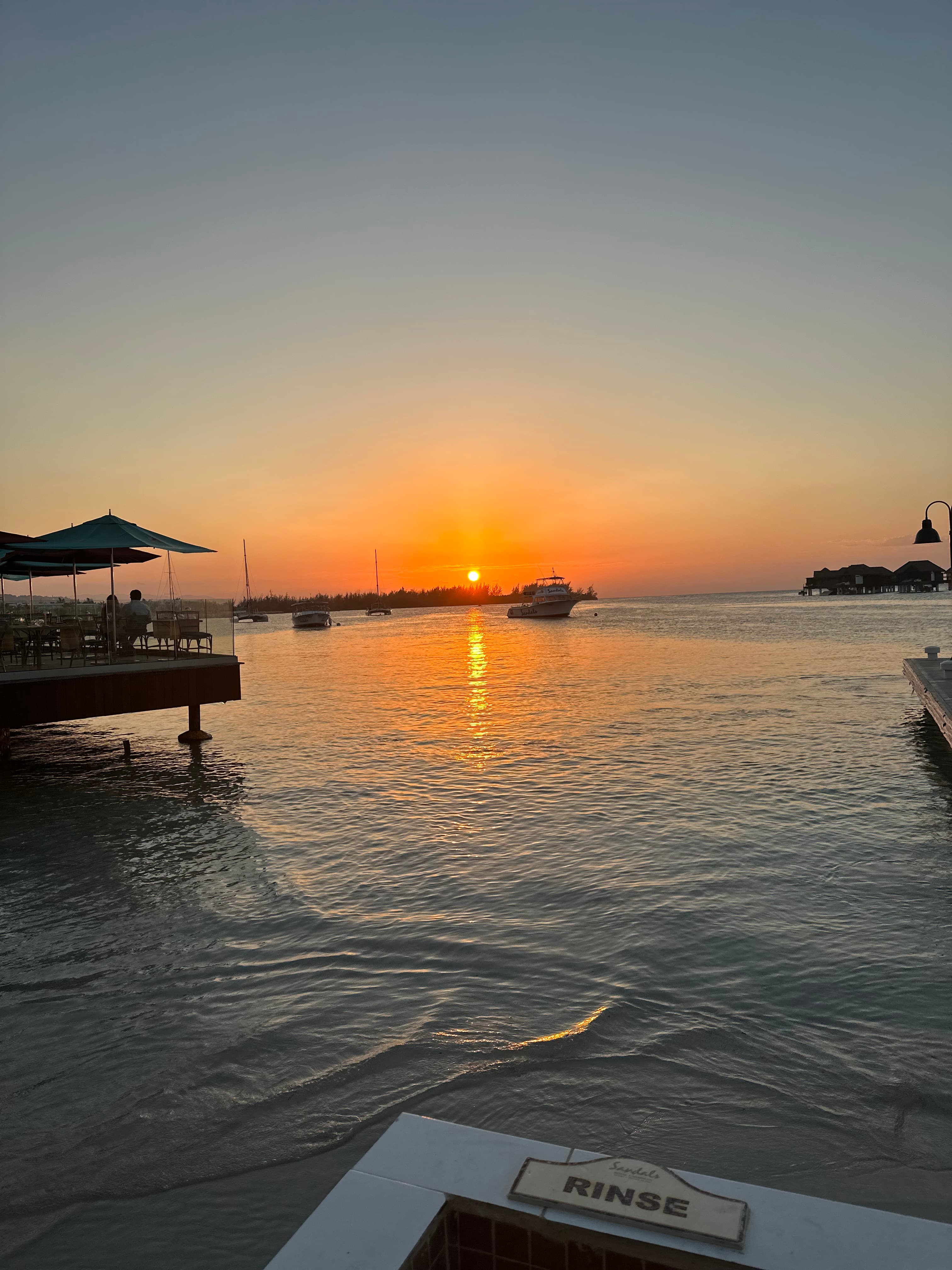 A picture of a sunset shining over the water with boats in the distance