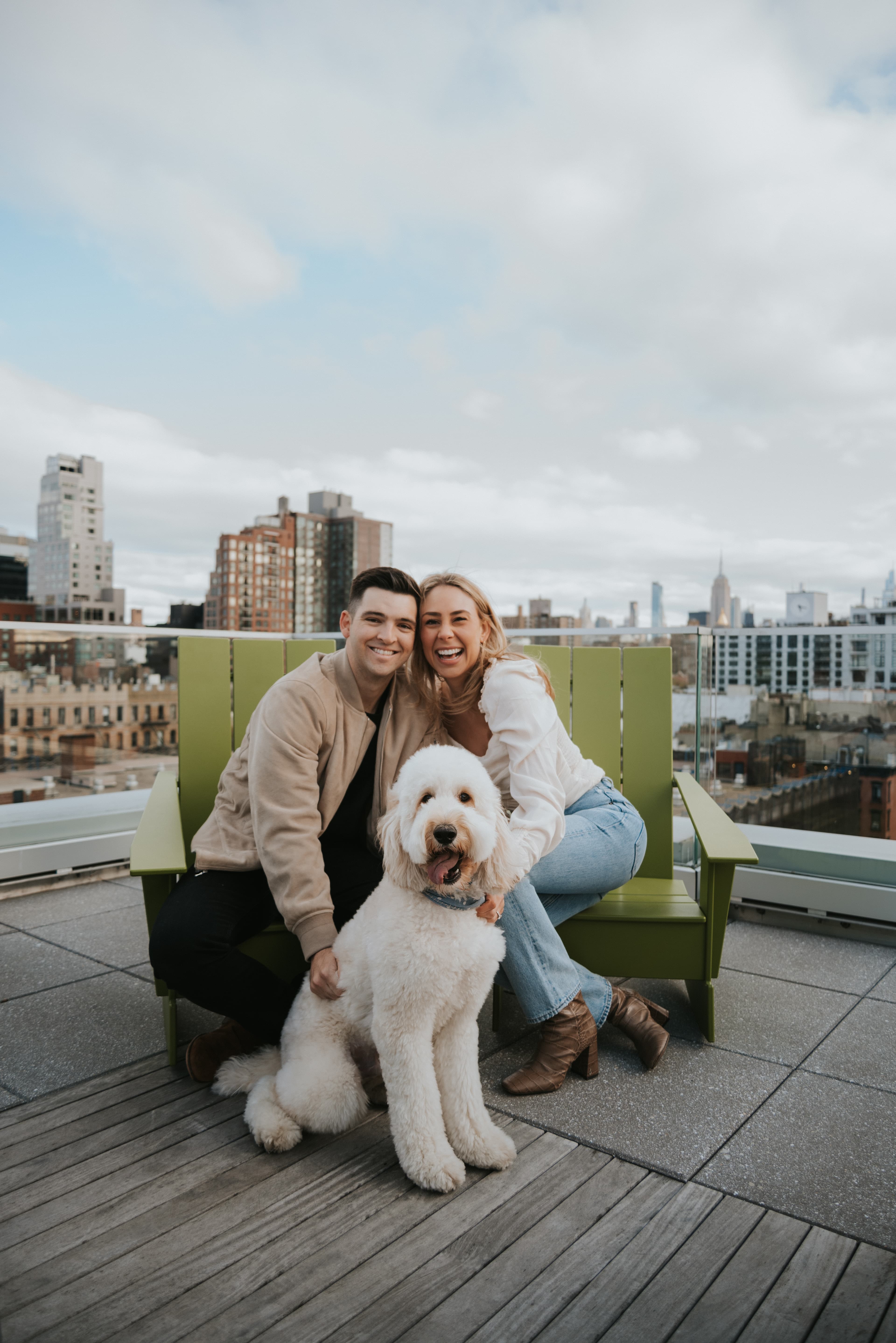 Couple posing in front of city skyline with their dog.
