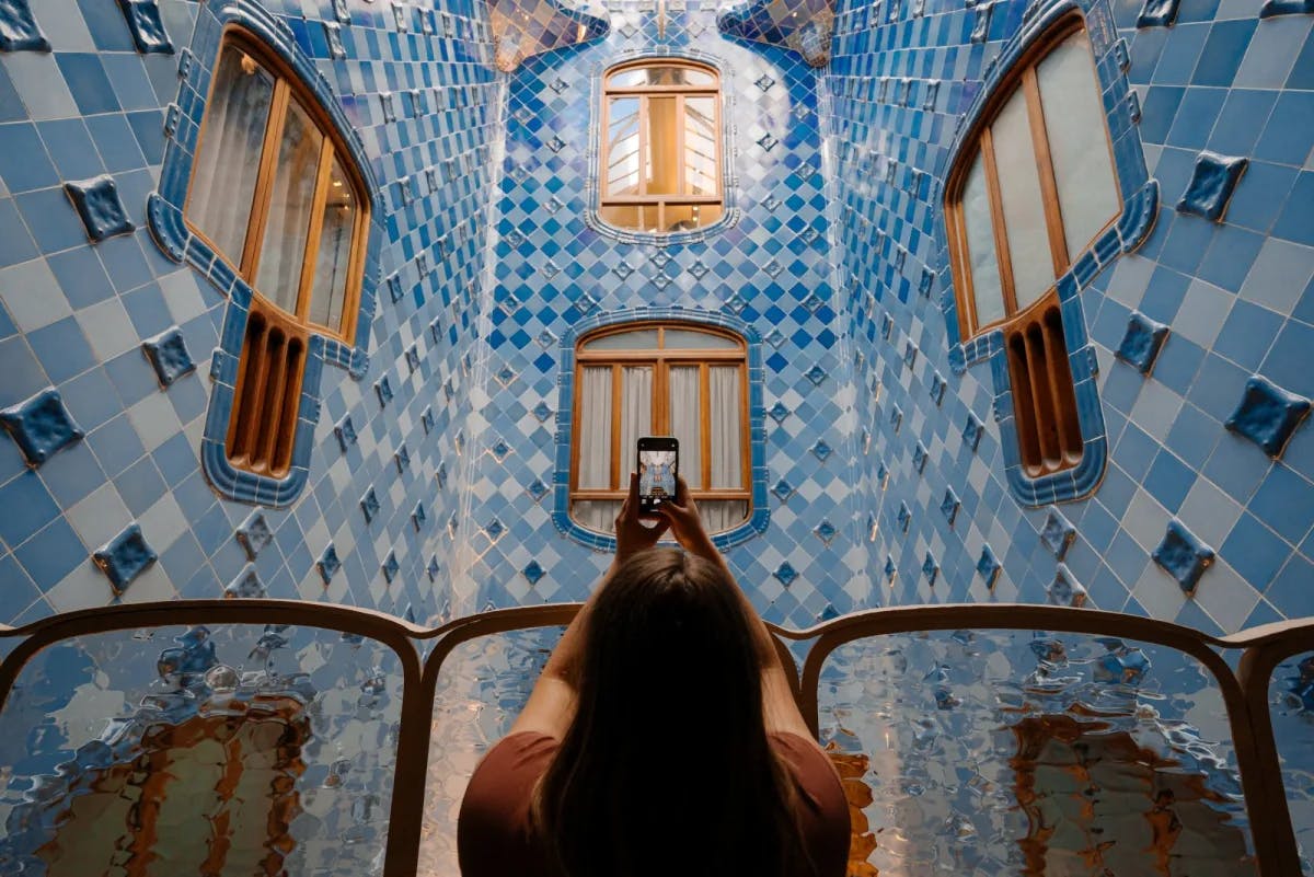 Somewhere in Barcelona, Spain, a young woman takes a photo of ornate, blue-tiled architecture with her phone