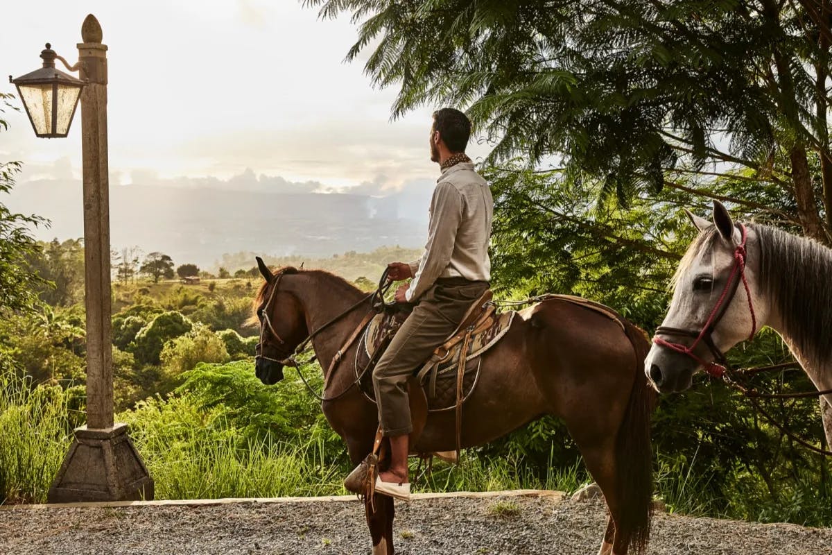 A man on horseback looks out over vast swathes of lush Costa Rican jungle from a vantage point at Hacienda AltaGracia, Auberge Resorts Collection