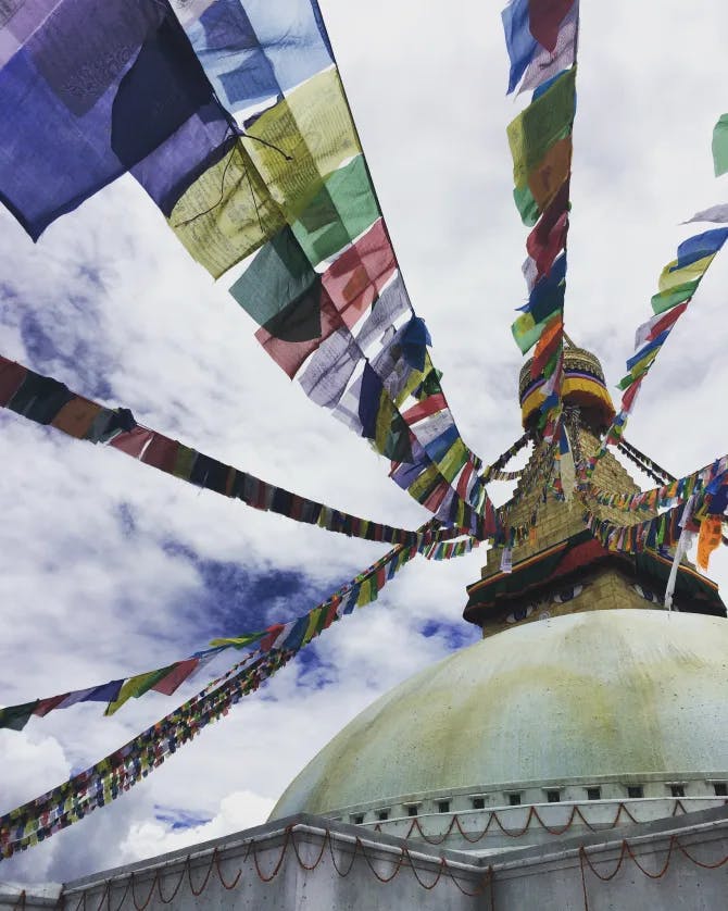 A picture of Buddha Stupa complete with colorful flags and a cloudy sky in the background