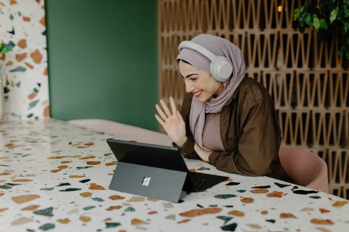 A woman in a hijab teleconferences on her computer from what appears to be her trendy home office