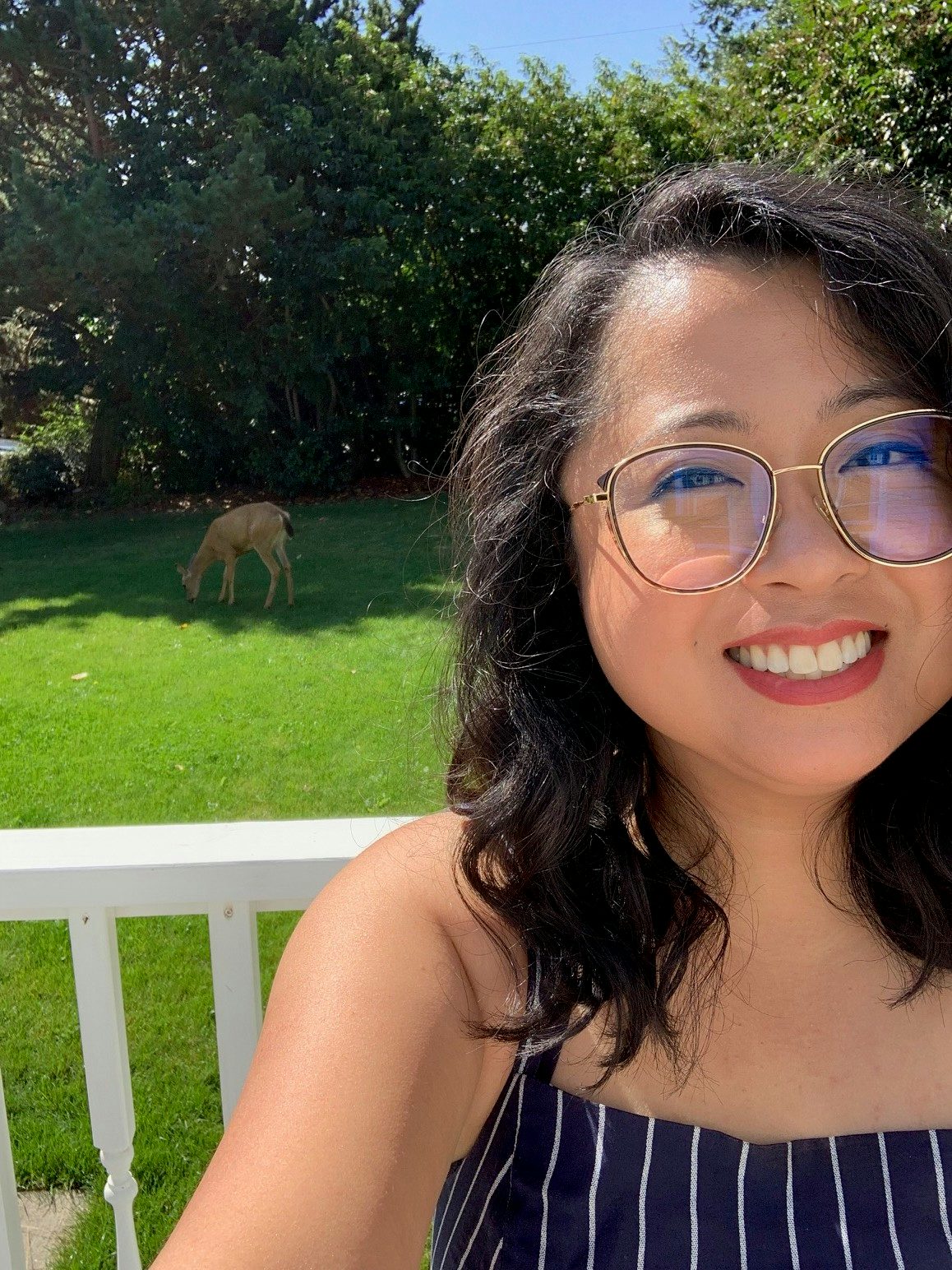 Travel advisor Jennyl Calugas wears a striped navy and blue top and smiles in front of a backyard with a dog in the grass