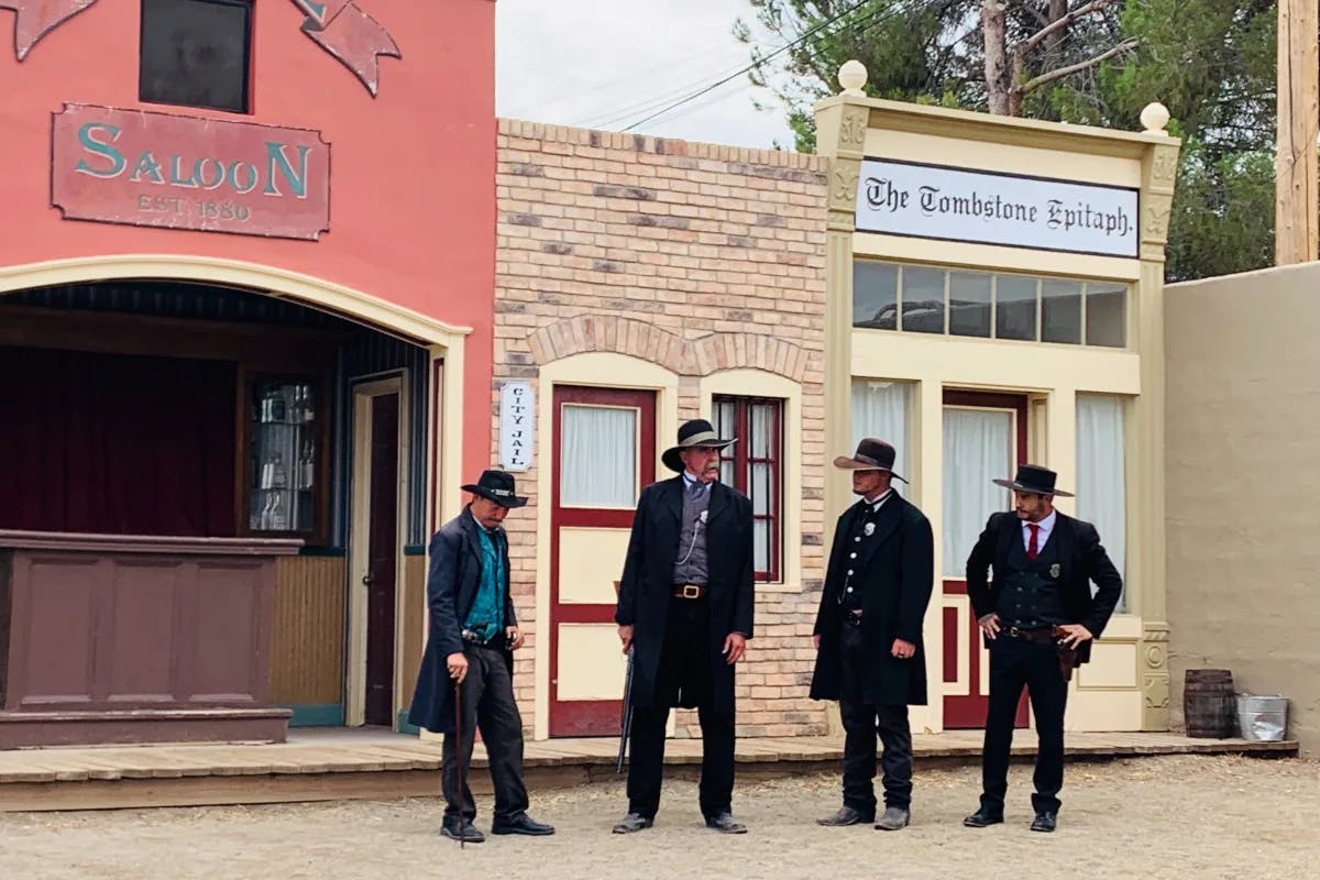 Men with hats and long coats standing outside a vintage saloon.