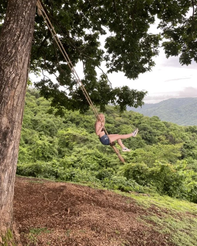 Swinging on the swing outside above dirt and grass with trees and a mountain in the background