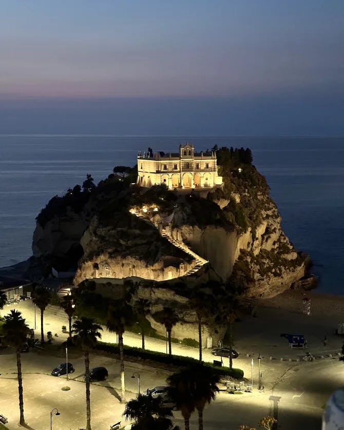 A hotel lit up on the top of a hill overlooking the sea at night 