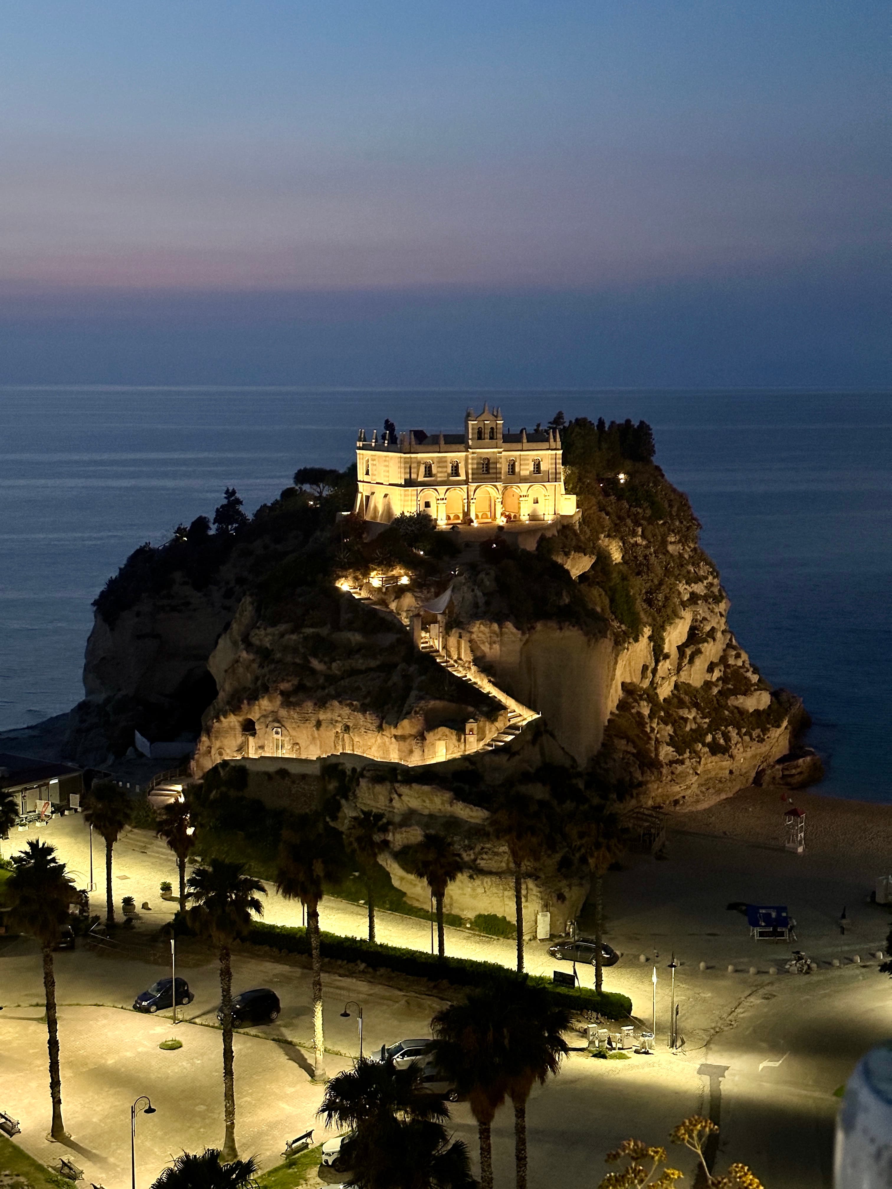A hotel lit up on the top of a hill overlooking the sea at night