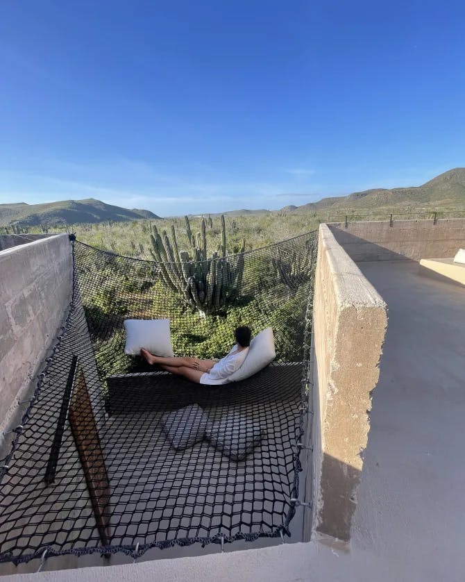 A view of a sitting area with a person lounging near a cactus and valley from Paradero hotel in Mexico