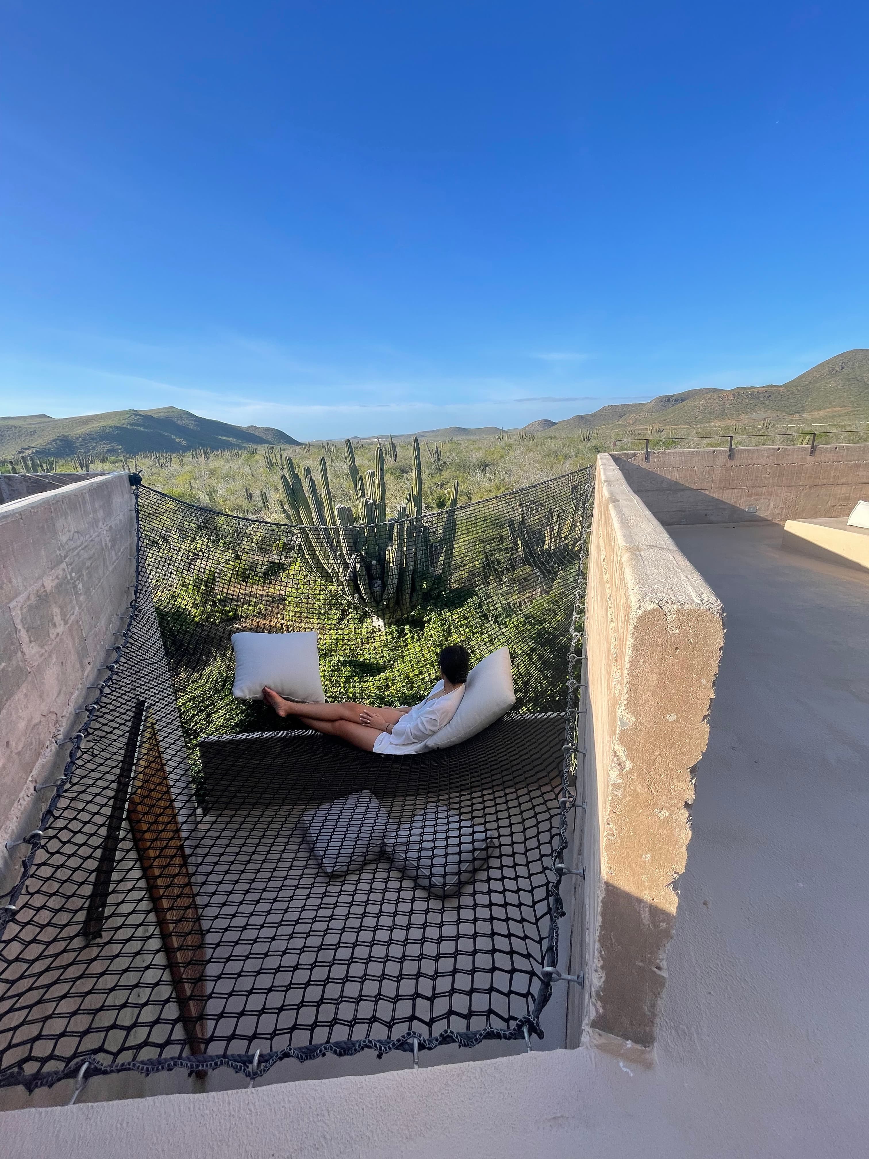 A view of a sitting area with a person lounging near a cactus and valley from Paradero hotel in Mexico