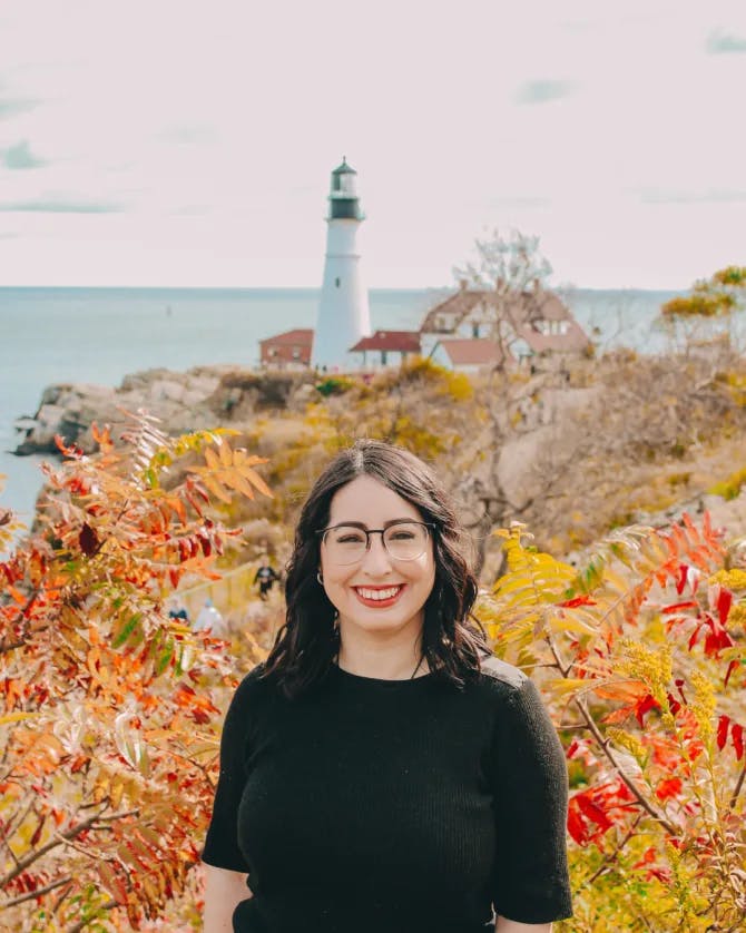 Travel advisor Sierra in front of fall foliage and a lighthouse on the coast.