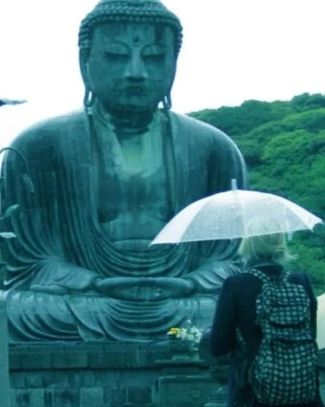 Carrie posing in the rain standing next to a large statue of Buddha 