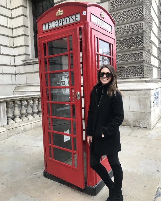 Picture of Shelby in a black dress standing next to a red telephone booth in London