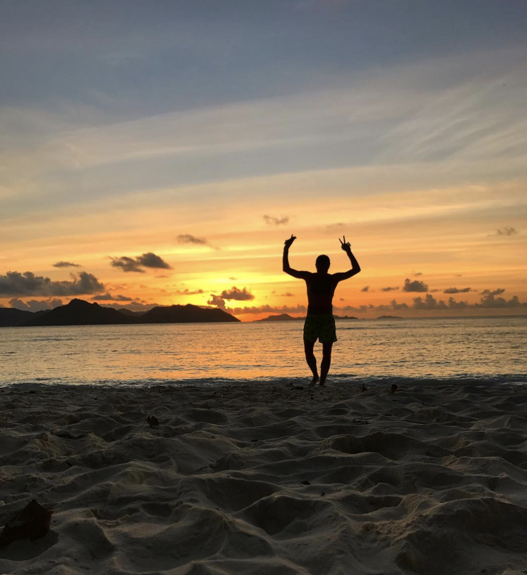 Person posing on the beach in front of colorful sunset