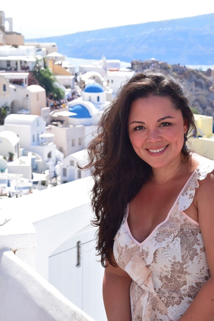 Travel advisor Jamielys Ponce de Leon in a floral top standing in front of the white hillside buildings of Greece.