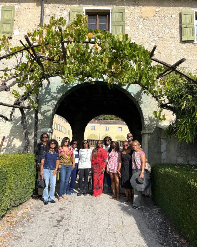 Nadeen and a group of travelers posing for a picture outside beneath a stone and vine covered archway. 