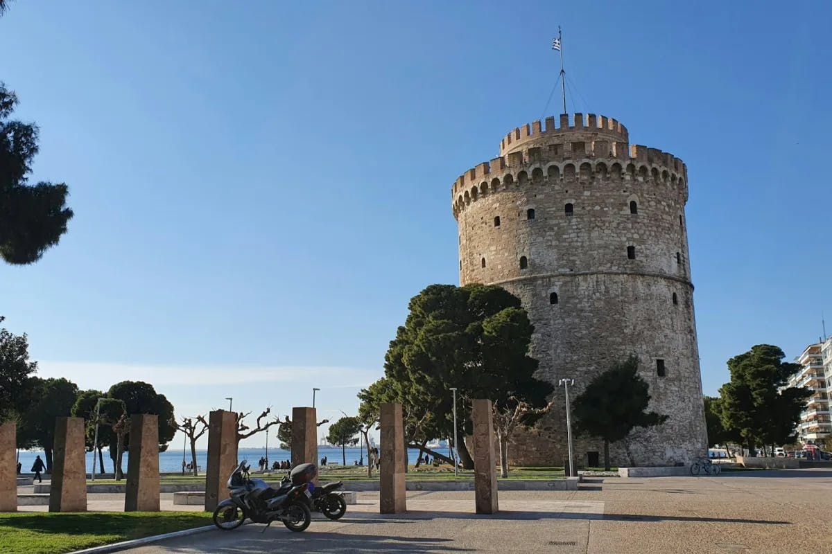 A stone parking lot with a couple motorcycles leads up to a medieval tower in Thessaloniki, one of the best places to stay in Greece