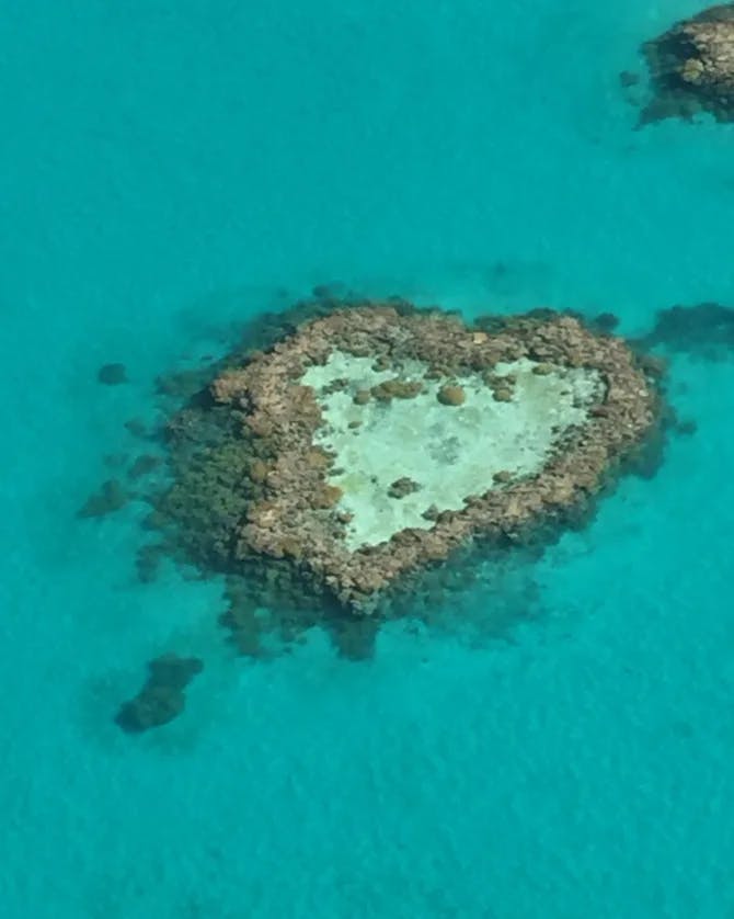 An aerial view of a heart shaped island surrounded by turquoise blue water