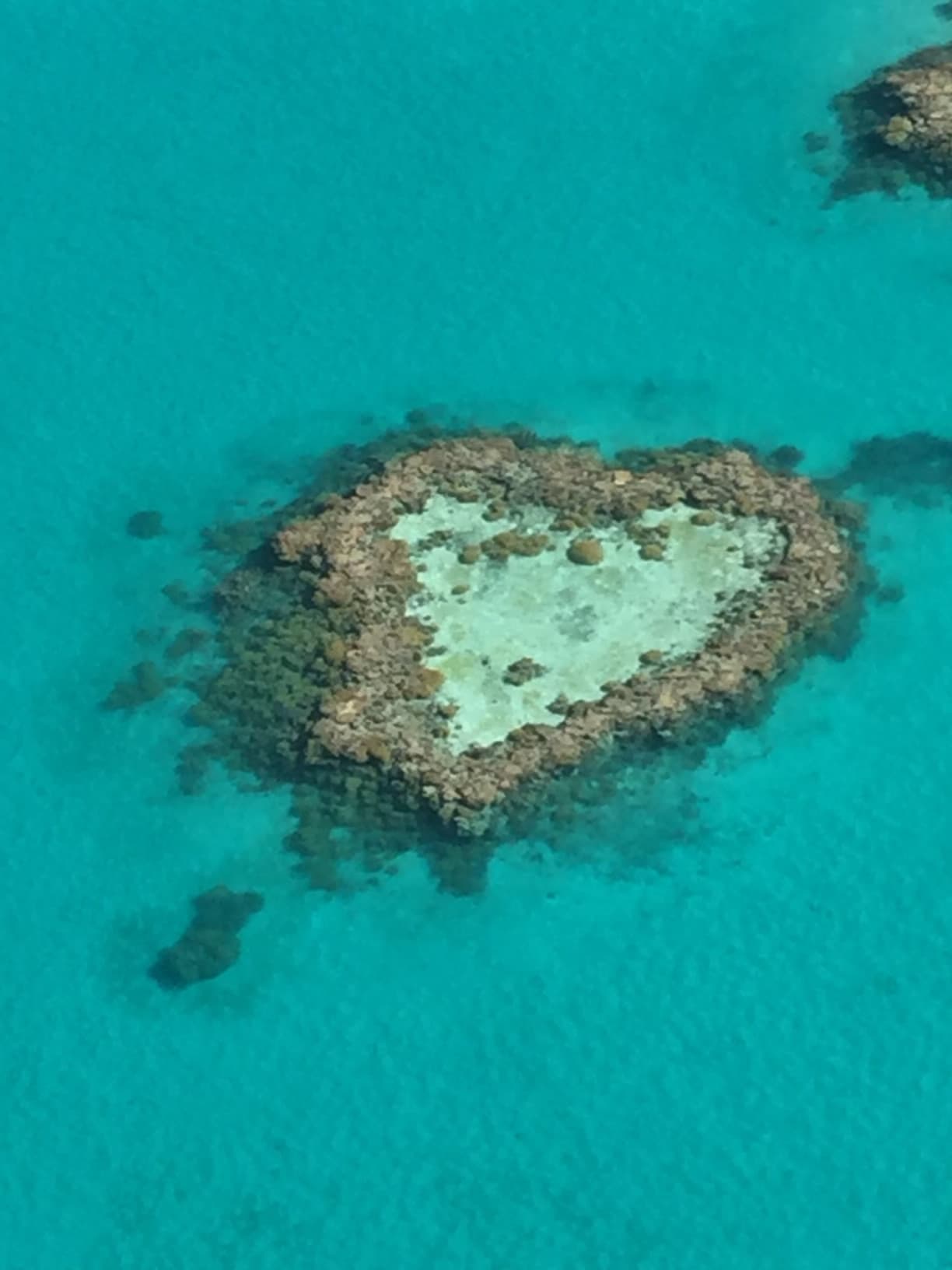 An aerial view of a heart shaped island surrounded by turquoise blue water