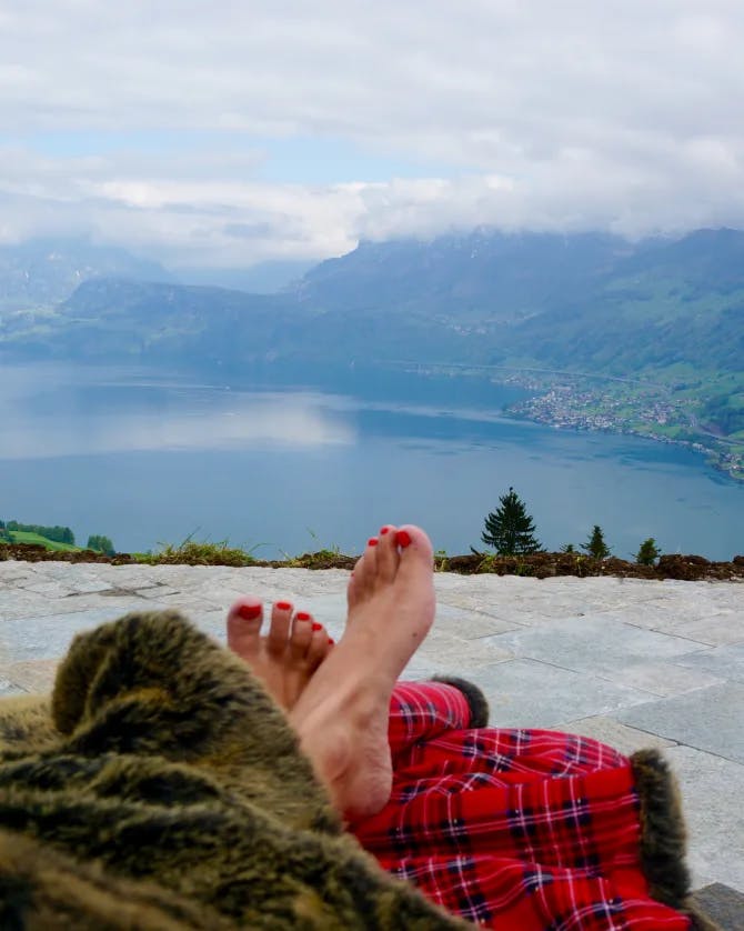 Kara lounging at Hotel Villa Honegg with a view of a lake and cloudy mountains in the distance
