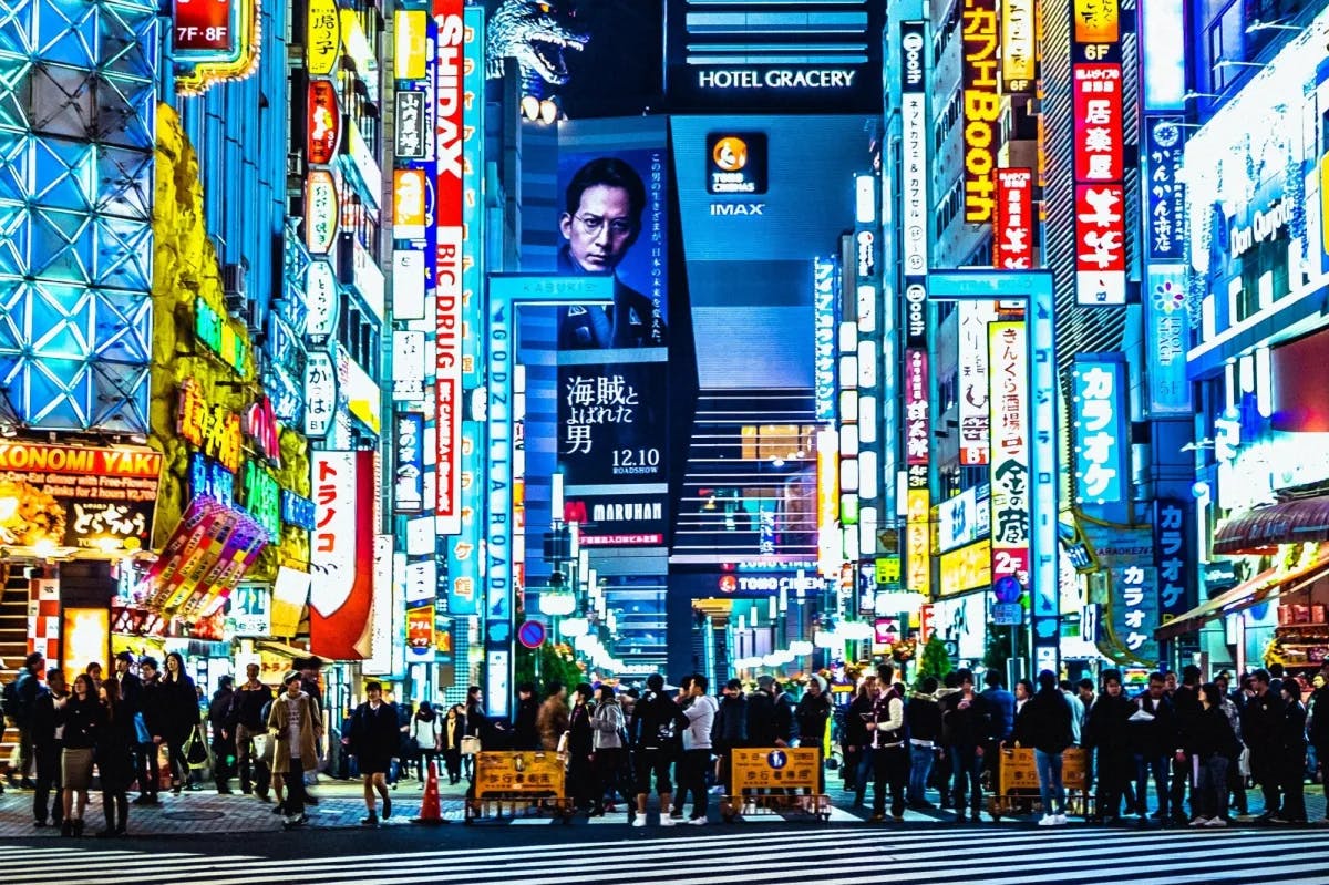 Thousands of travelers walk a narrow, neon-sign-filled street in Tokyo, Japan