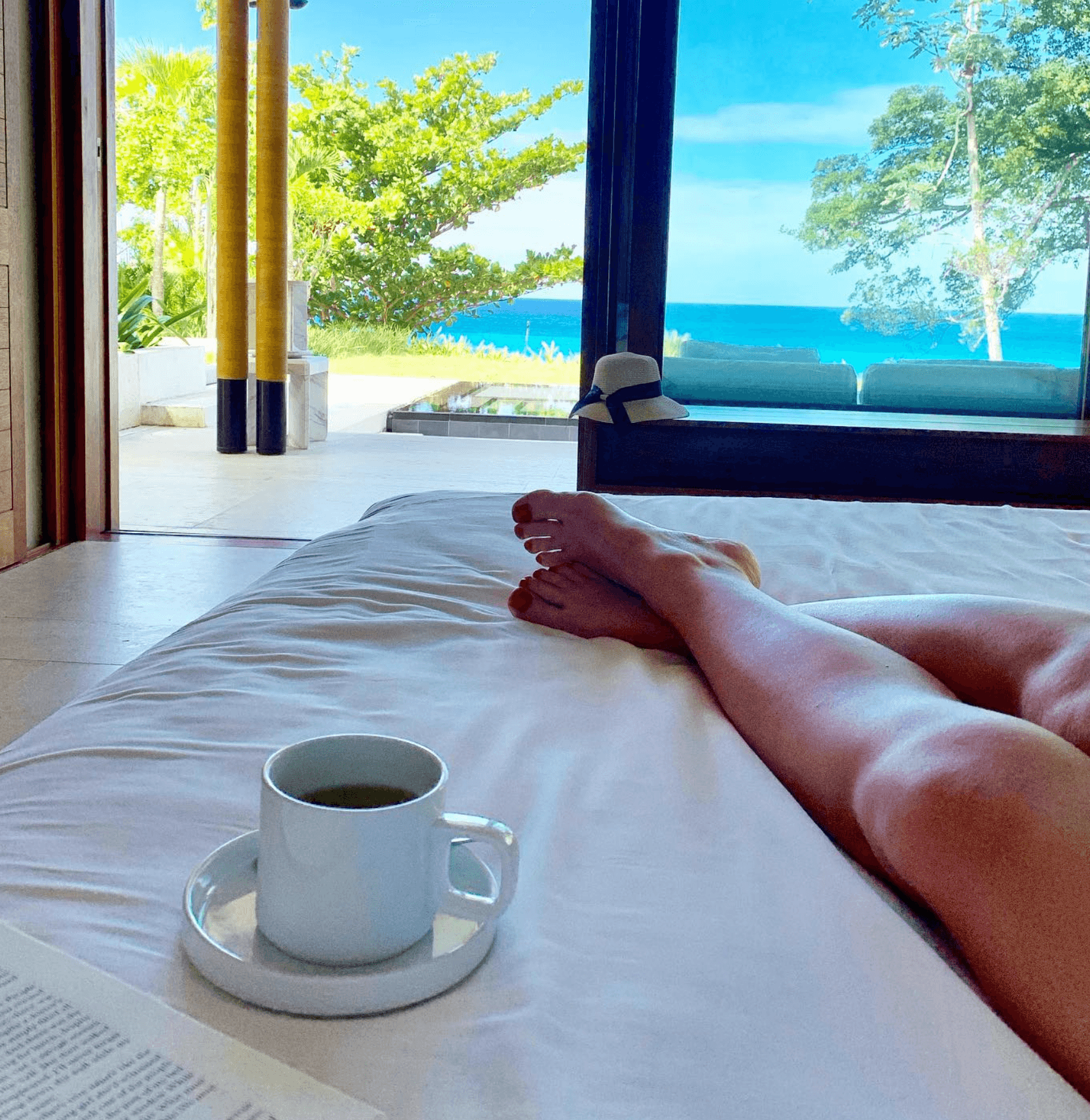A person having tea in bed with view of the ocean outside their window.