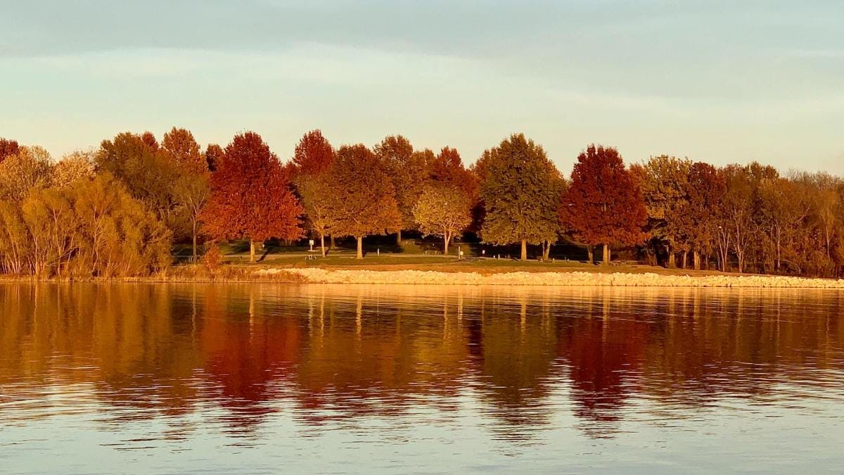 Fall foliage of red, auburn and orange trees reflecting on clear lake in Missouri.