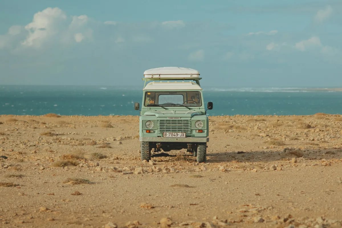 A vintage Land Rover sits alone on a rocky beach 