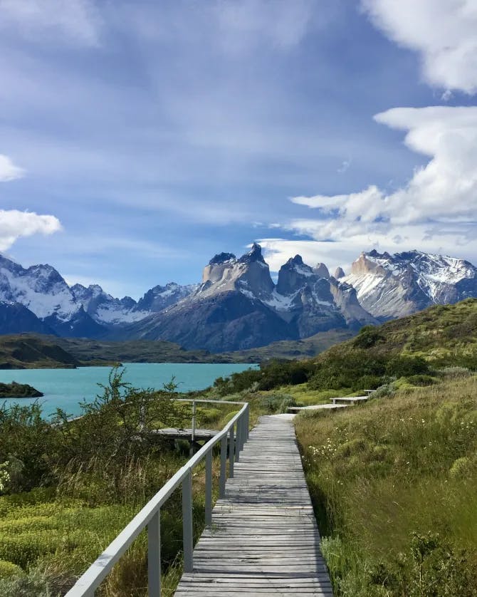A picture of Torres del Paine National Park with a wooden path that leads to turquoise blue waters and mountains in the background 