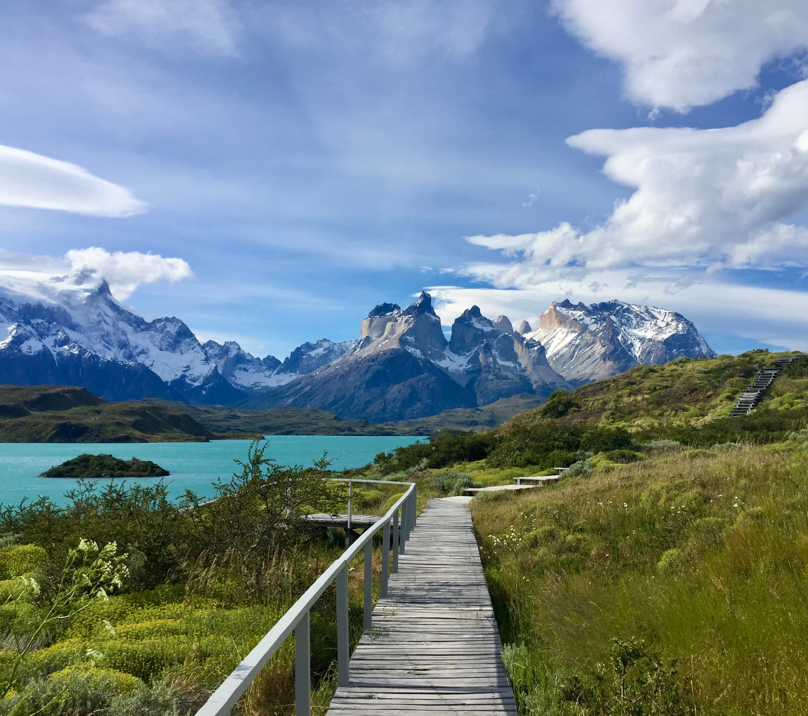 A picture of Torres del Paine National Park with a wooden path that leads to turquoise blue waters and mountains in the background
