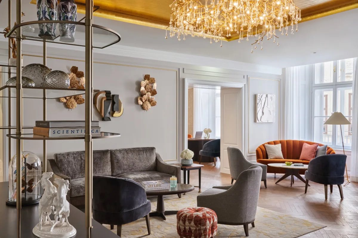 chic lobby area with a rounded orange couch, a tiered shelf with various knickknacks an books, as well as a lit chandelier
