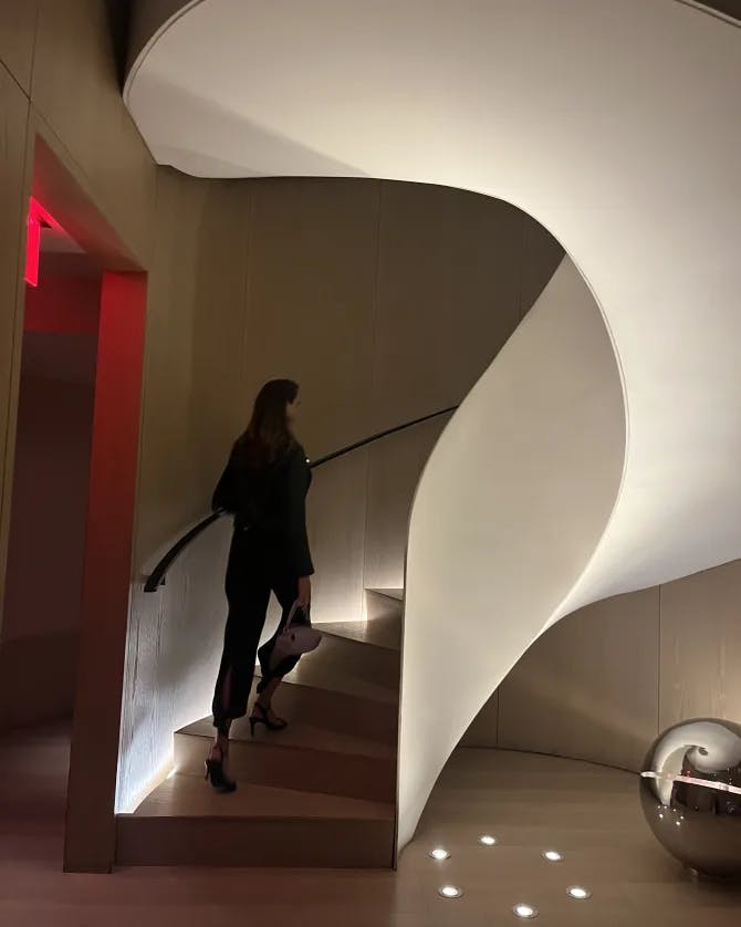 A person walking up an abstract white staircase with a red lit doorway to the left of them