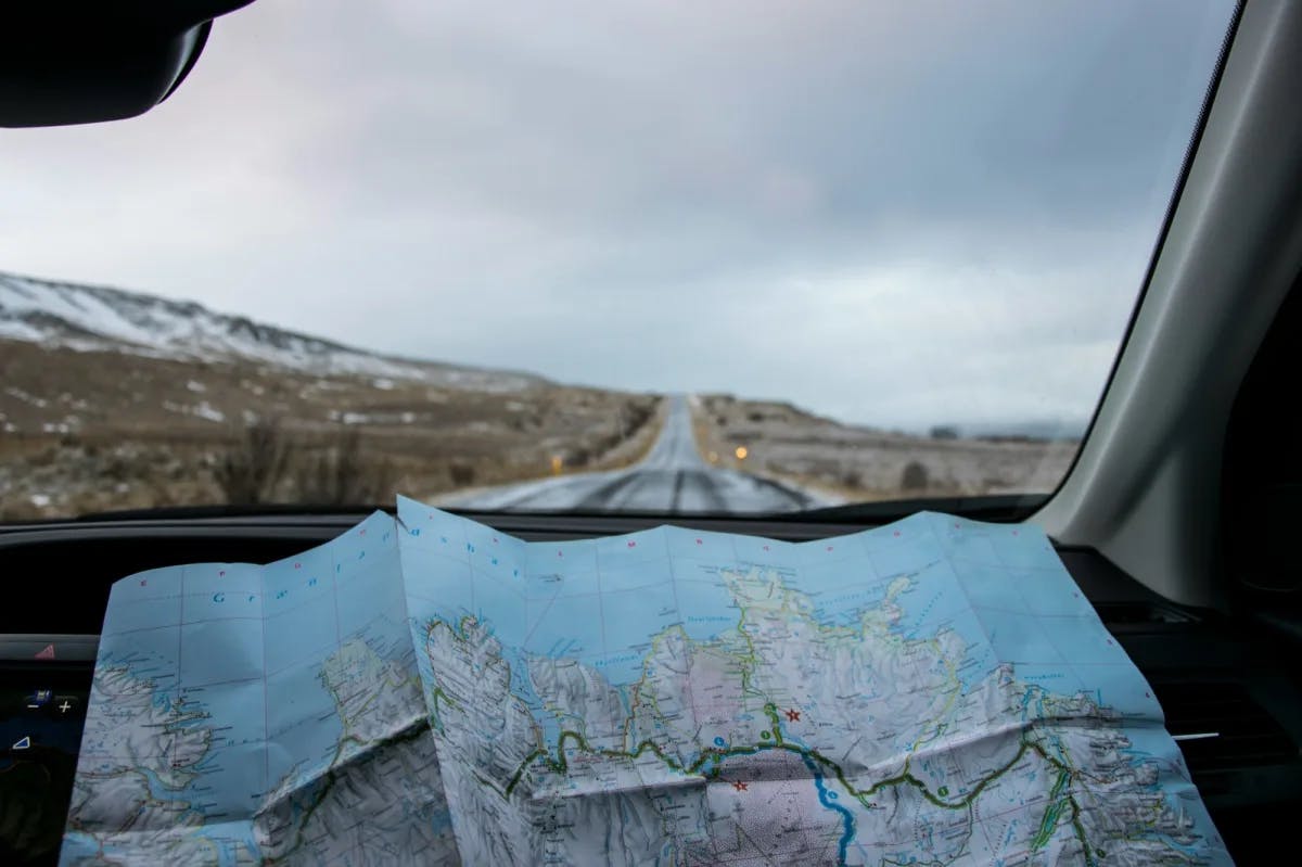 View from the passenger seat of a vehicle, a map is laid out in the foreground while an icy road lies ahead