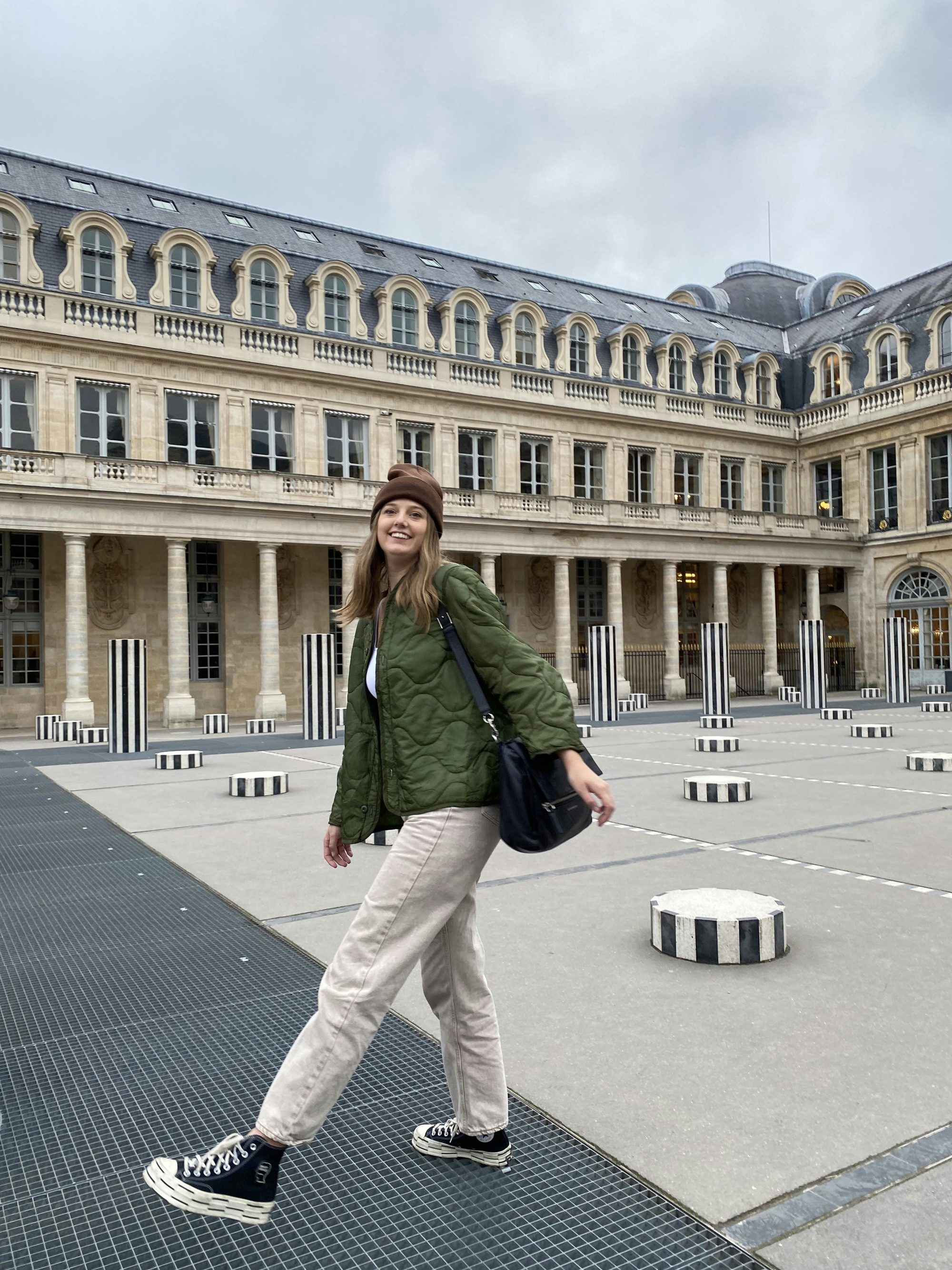 Travel Advisor Savannah Baker wears black covers and a army green coat in a Parisian courtyard. 