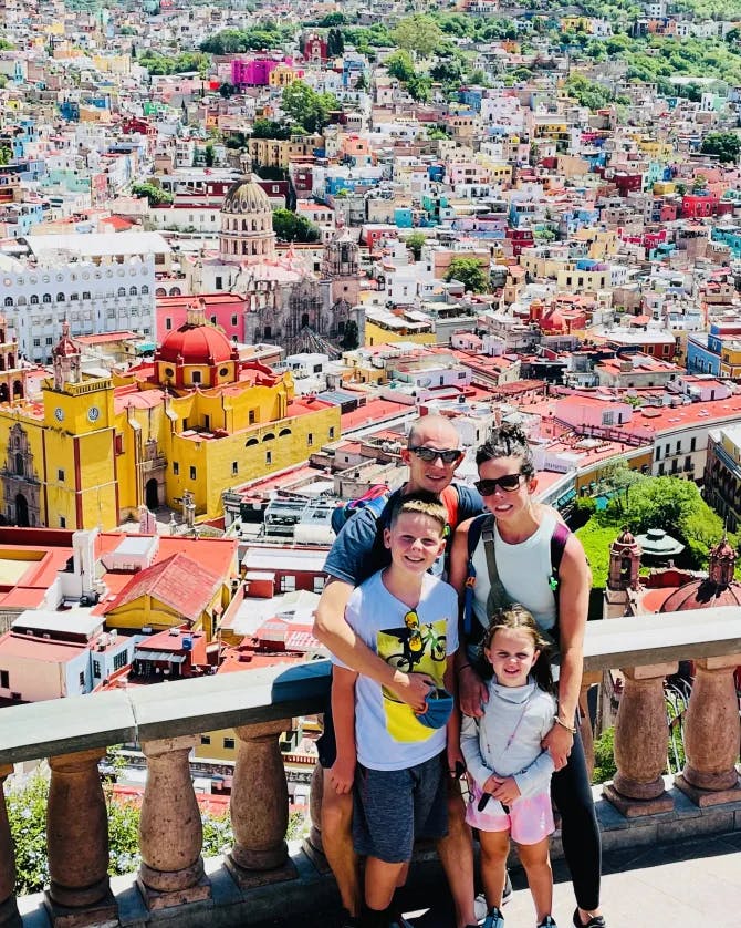Samantha and family posing for a photo on a balcony in front of a vibrant city landscape
