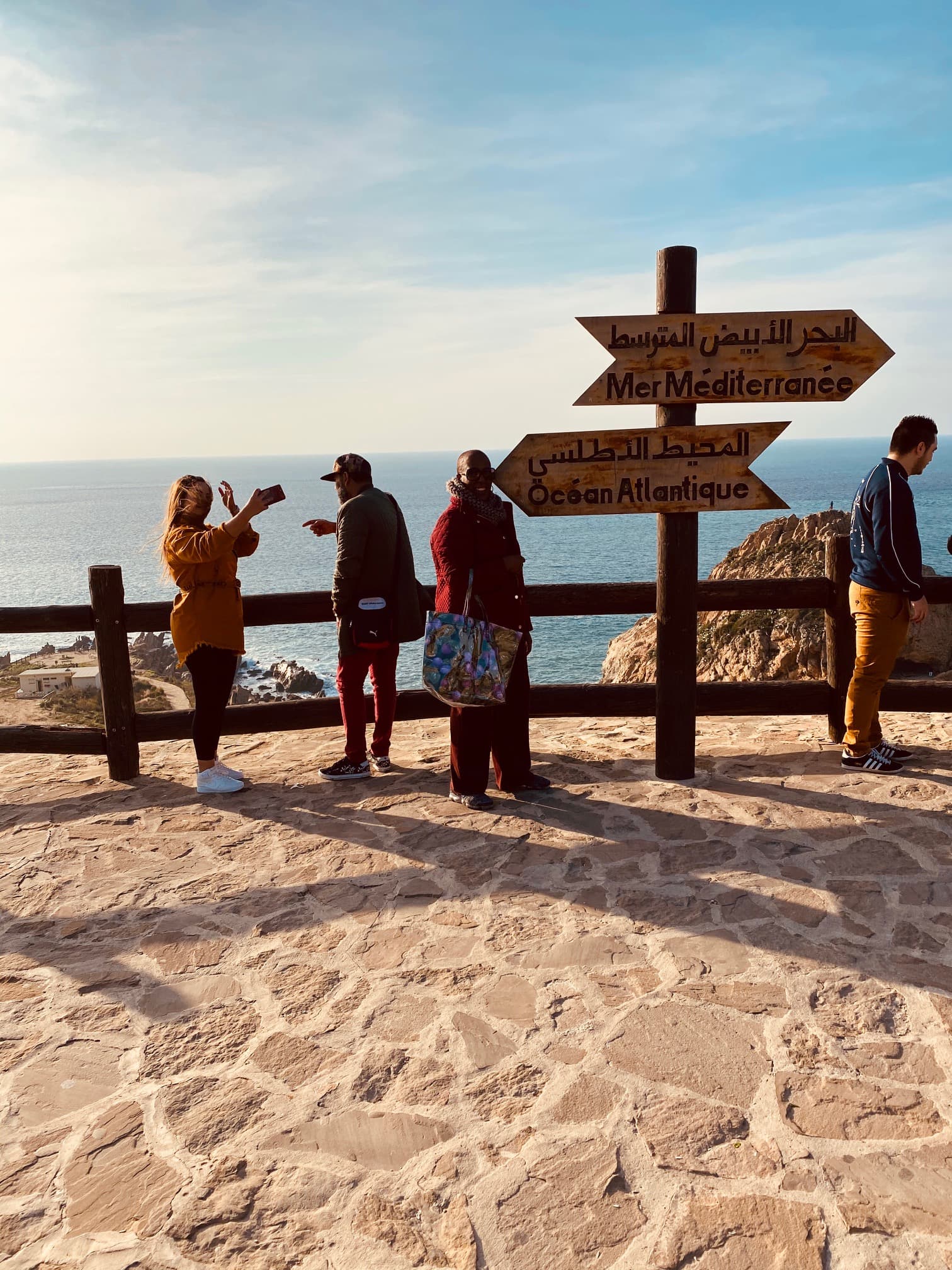 people standing on a stone path next to a fence overlooking the sea