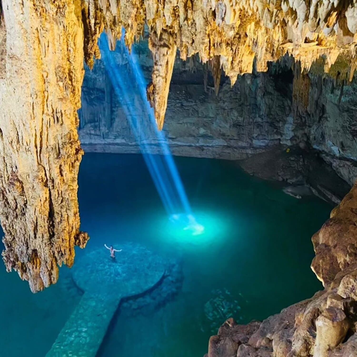 Picture of Cenote Suytun, a cave with a hole in the roof, shining a beam of light onto blue water