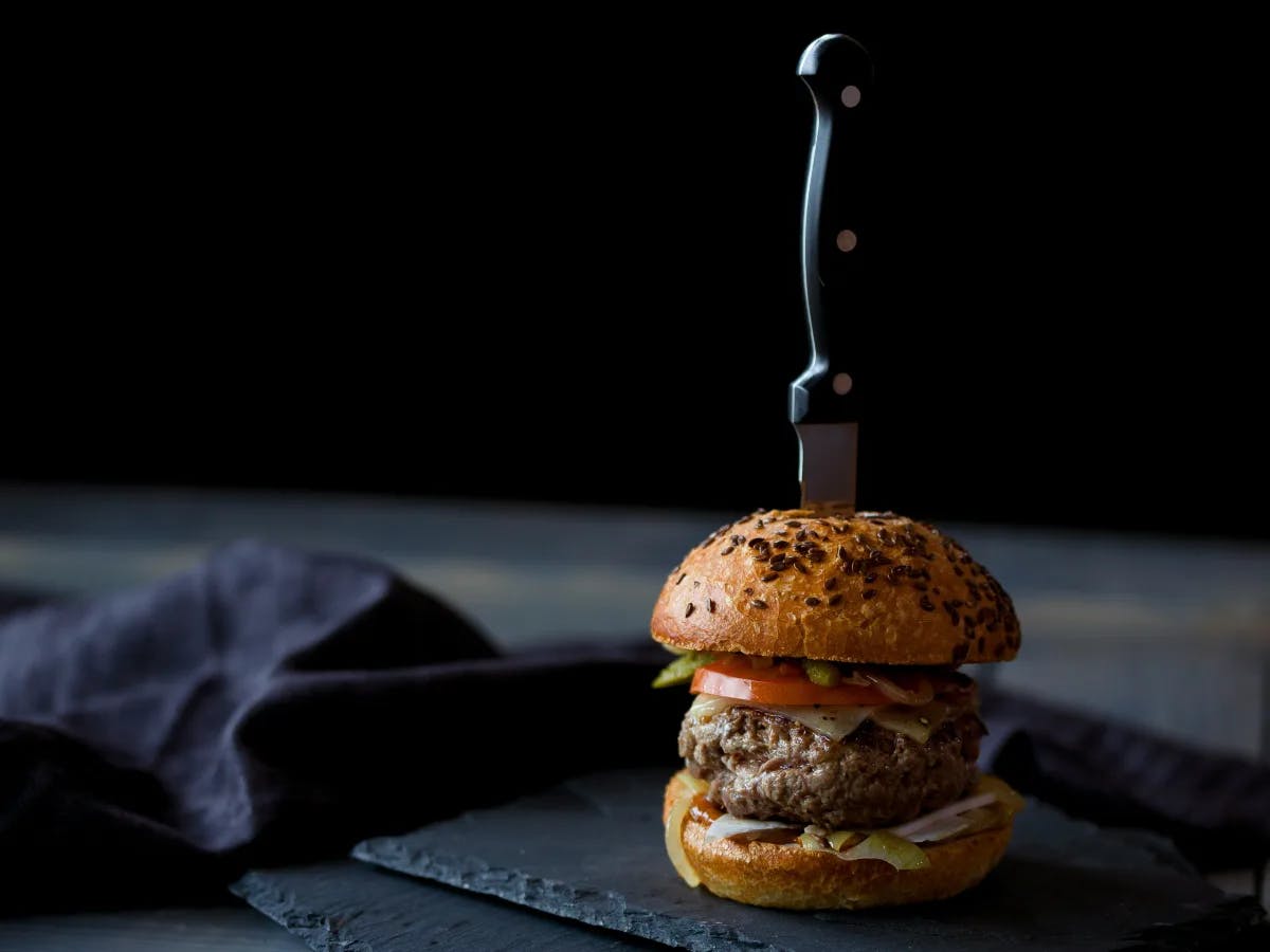 A gourmet burger on a slate board, pierced with a knife.