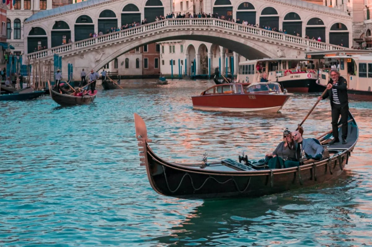 A gondolier paddles a couple through a historic canal in Venezia, Italy