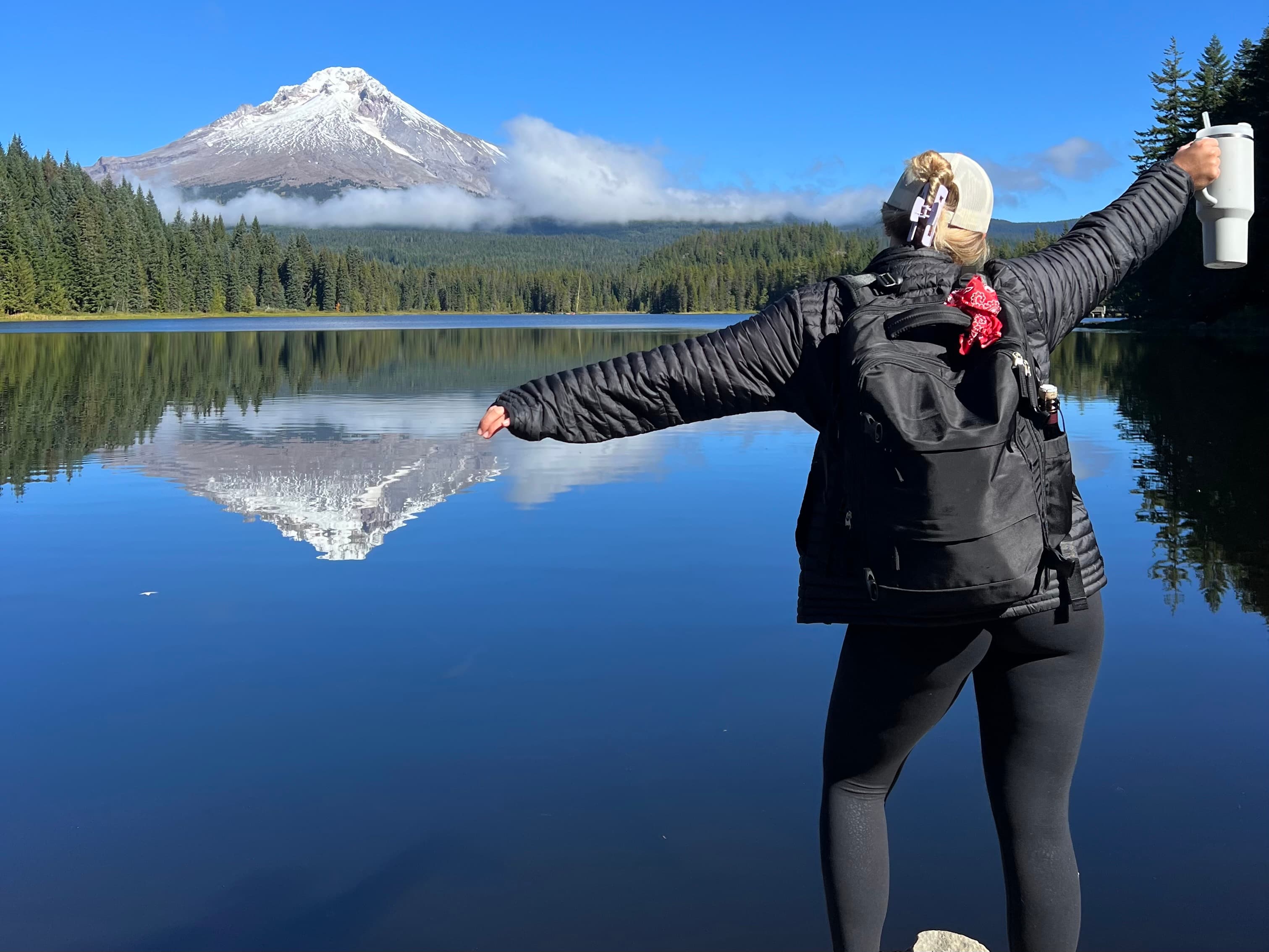 brittany posing for a photo facing a beautiful mountain scape with snow covered tops and a clear blue lake ahead with foliage.