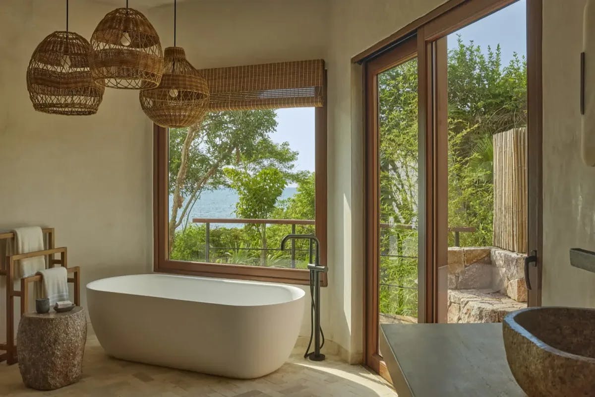 a fancy bathroom with wooden light fixtures and large windows overlooking the sea and jungle