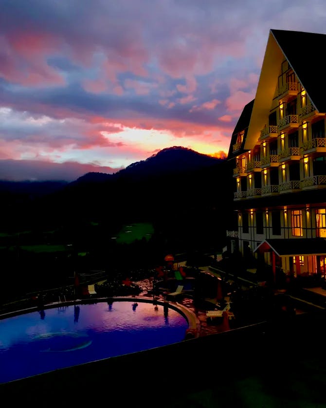 The Swiss-BelResort Tuyền Lâm hotel at dusk beneath a pink, blue and yellow sunset