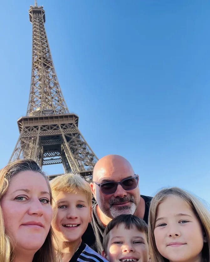 Karyn and her family posing in front of the Eiffel tower with clear skies in the distance. 